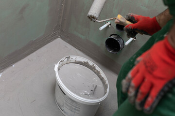A professional worker soaks a paint roller in a bucket with moisture insulation. Protective glove.