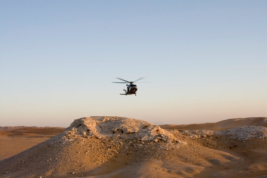 A helicopter in the desert flying low to the ground and rocks