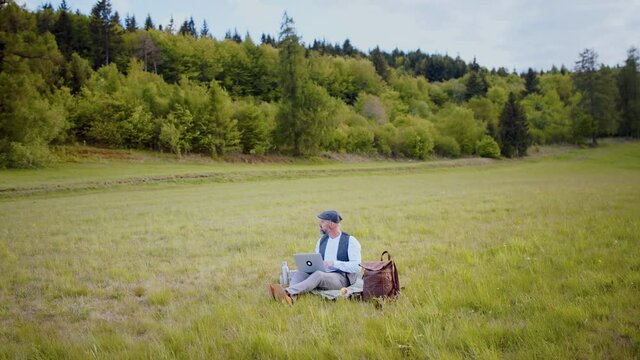 Mature man with laptop on meadow in nature, outdoor office concept.