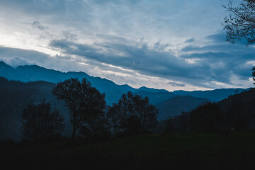 Aerial/Drone View of a foggy Himalayan valley and green fields surrounded by lush green hills during a beautiful morning at a rural location in Uttarakhand, India.