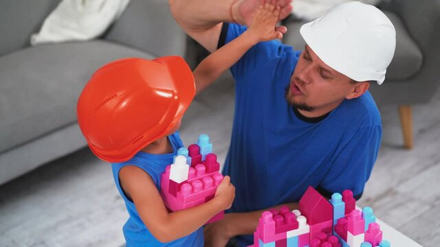 Top view of a son giving hi 5 to father wearing construction helmets playing brick constructor turn on camera and smile. Father and son concept. June 2019.Kiev, Ukraine. Prores 422.