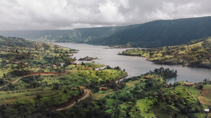 Obraz premium Aerial/Drone View of a river valley and an offbeat holiday resort in green surroundings during Monsoon season in Maharashtra, India.