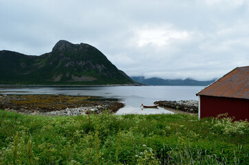 old red boat house with cloudy mountain range background and small docked boat