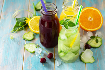 Summer various refreshments drinks. Cherry juice, detox cucumber water and orange juice on blue...