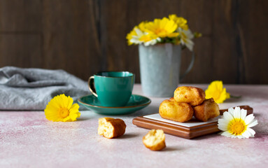 Fototapeta na wymiar A cup of coffee or tea with small sponge biscuits, traditional French madeleines cakes, white and yellow wildflowers on the table