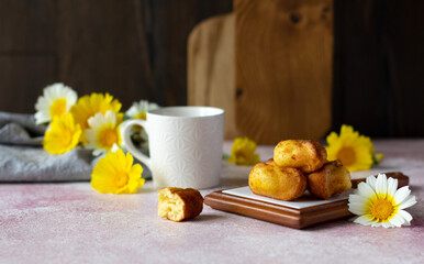 A cup of coffee or tea with small sponge biscuits, traditional French madeleines cakes with cup of tea, white and yellow wildflowers on the table. Breakfast or tea time concept