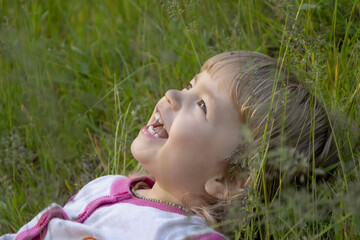 Portrait of a little girl lying on her back in the long grass and laughing.