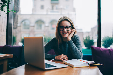 Smiling attractive student spending free time in coffee shop interior on exam preparation