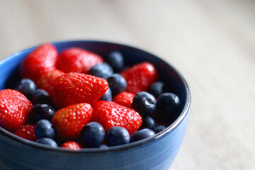 Bowl of blueberries and strawberries on a wooden table. Selective focus.