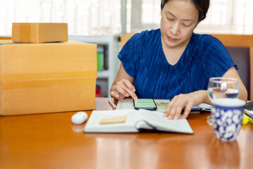 Woman checking order in cell phone online shopping store for delivery package to customer from home office.