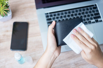 Woman cleaning money wallet and gadgets by wet wipes tissue and alcohol disinfectant on workplace during work at home, protection coronavirus (Covid-19) infection. New Normal and Clean surface concept
