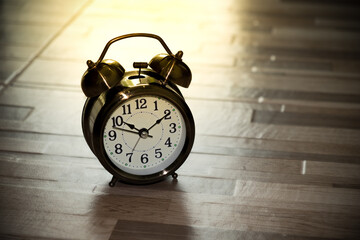 Vintage alarm clock on wooden floor with lighting effect.