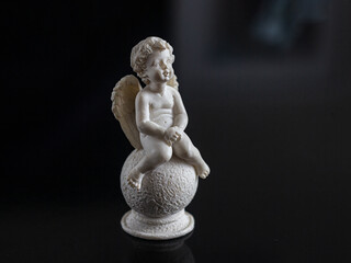 Small, sitting, plaster angel with wings, on a black background