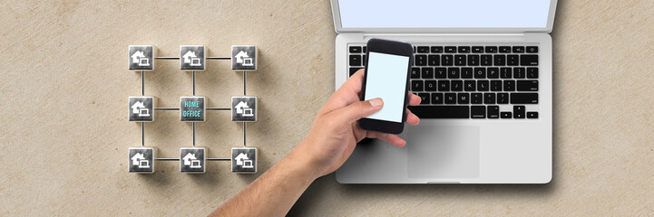 cube grid with message HOME OFFICE and hand with smartphone over laptop on paper background