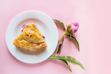 Top view of piece of cherry pie with peonies flowers on a pink background