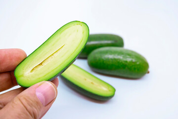 Three mini avocados on white background. Close up on hand holding a half sliced avocado without seed. A special cultivated exotic green vegan food for healthy living.