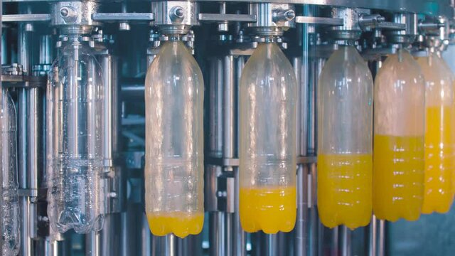 Transparent plastic bottles move on conveyor belt and filled of juice 