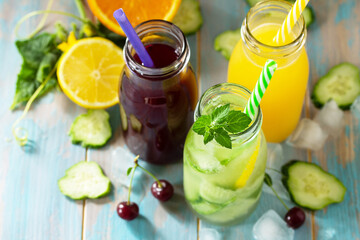 Summer various refreshments drinks. Cherry juice, detox cucumber water and orange juice on blue wooden table.