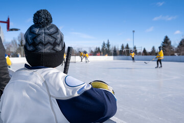 Young Hockey Player watching outdoor ice hockey game from behind the boards