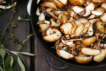 Close-up forest mushrooms, potatoes, onions and seasonal herbs in a cast iron pan on a wooden background outdoors