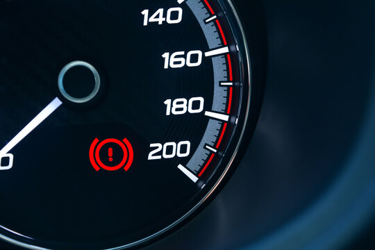 the screen of black car's gauge with white number of speed level and red warning sign of handbrake
