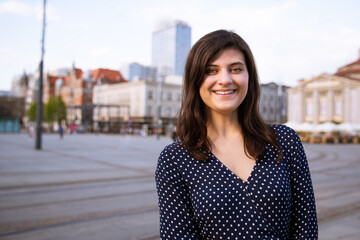 Cheerful young woman standing outdoors in the city and smiling at camera