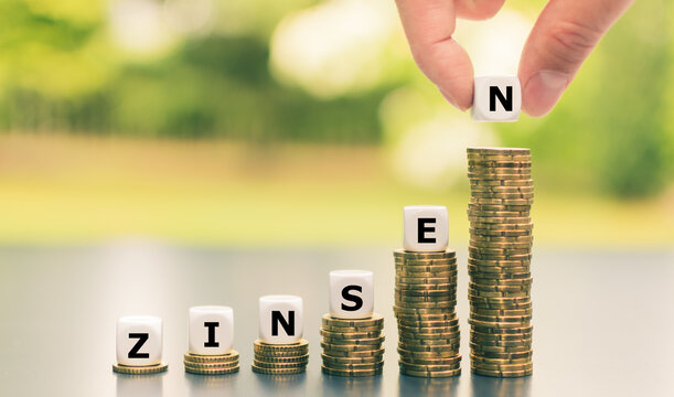Dice form the German word "Zinsen" ("interest rates") on increasing high stacks of coins.