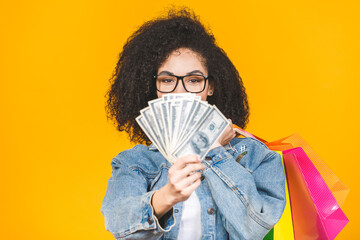 Shopping Concept - Portrait young beautiful african american woman smiling and joyful with colorful shopping bags and money isolated over yellow Background. Copy Space.