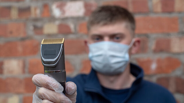 A Barber Hairdresser Showing His Clippers Whilst Working Illegally In Lockdown During This Pandemic Frustrated Not Earning Money Self Employed, Safety Precautions Are In Black With Face Mask & Gloves