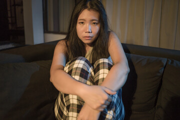 Fototapeta premium young beautiful sad and depressed Asian Japanese woman in pain at living room sofa couch crying helpless and desperate suffering depression