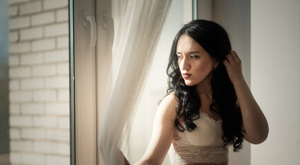 beautiful girl with long black hair in a lace dress against the window