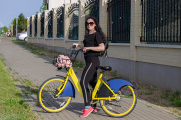 Fototapeta na wymiar Nice smiling girl in sports wear with yellow bike in summer street