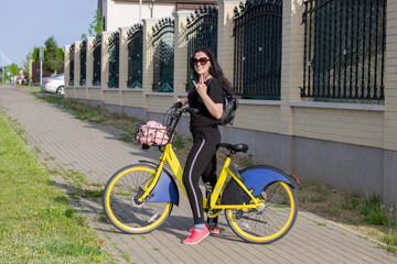 Fototapeta na wymiar Nice smiling girl in sports wear with yellow bike in summer street