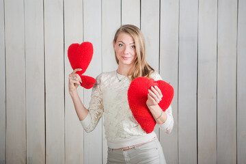 beautiful young blonde woman looks at camera holding many red heart shaped pillows