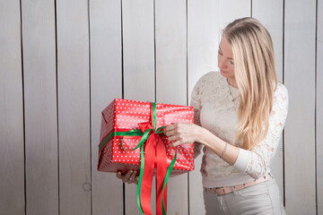 closeup young pretty slim blond girl looks at large red gift box holding in hands