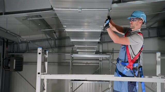 Caucasian Male Air Conditioning Professional Assembling Ventilation Duct On Ceiling Of Interior Of Large Building. 