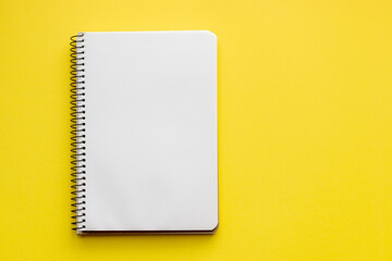 Spiral notebook with blank empty white sheets on a bright yellow background, top view, flat lay with copy space