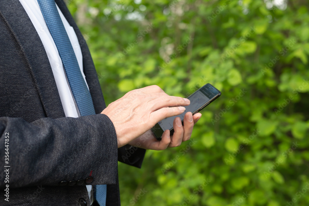 Poster businessman using mobile smart phone in the park. man in suit with blue tie searching the internet o