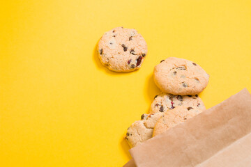 homemade cookies with pieces of chocolate and lingonberries in a paper bag on a yellow background copy space healthy snack on the go concept
