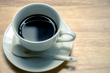 Black coffee in a coffee cup on wooden blurred background.