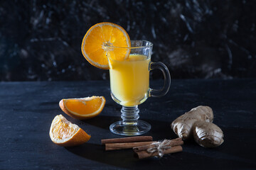 Orange juice with ginger in a glass mug, ginger, cinnamon on a black background. Freshness. Detox.