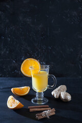 Orange juice with ginger and cinnamon in a glass mug, on a black background. Freshness. Copy spaes.