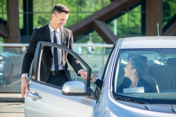 Man standing near open door of car, woman sitting inside.
