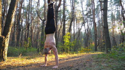 Muscular man doing handstand at beautiful sunny forest. Strong gymnast training in scenic environment. Athlete showing performance outdoor. Concept of healthy and active lifestyle. Slow mo Close up