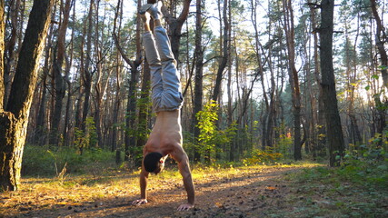 Muscular man doing handstand at beautiful sunny forest. Strong gymnast training in scenic...