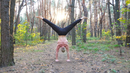 Young man doing handstand at beautiful sunny forest. Strong gymnast training in scenic environment....