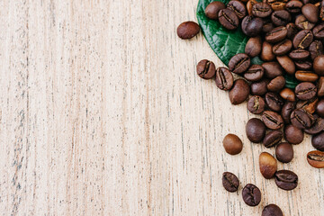 Coffee beans on a green leaf and scattered on a light wooden table, top view, closeup grains, flat lay, place to insert text, copy space