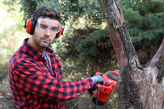 Young man cutting trees with electric chainsaw 
