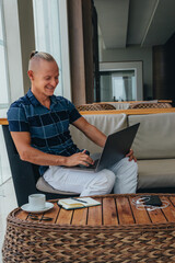 smiling guy is reading mail on a laptop, with a cup of coffee. The student makes a note. Types the text of the message to reply