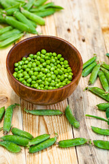 closeup green peas in brown dish, on wooden table.